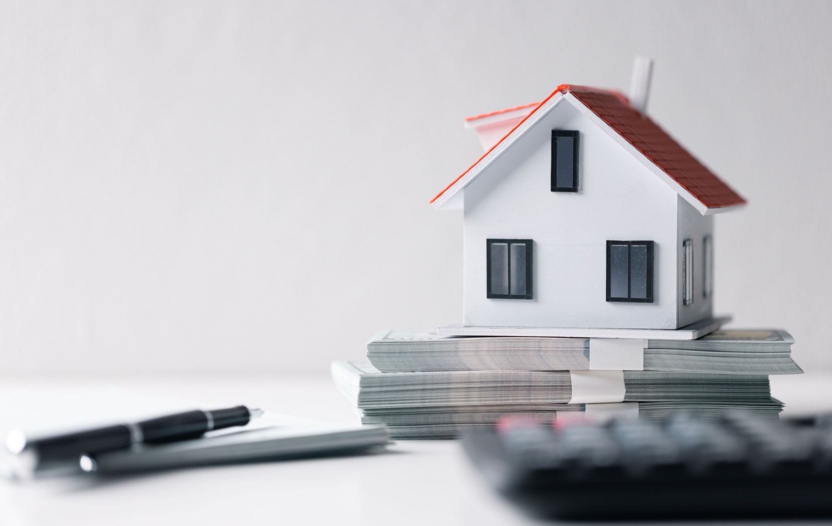 A toy house sits on a stack of money with some paperwork to represent the equity that could be unlocked through mortgage refinancing.