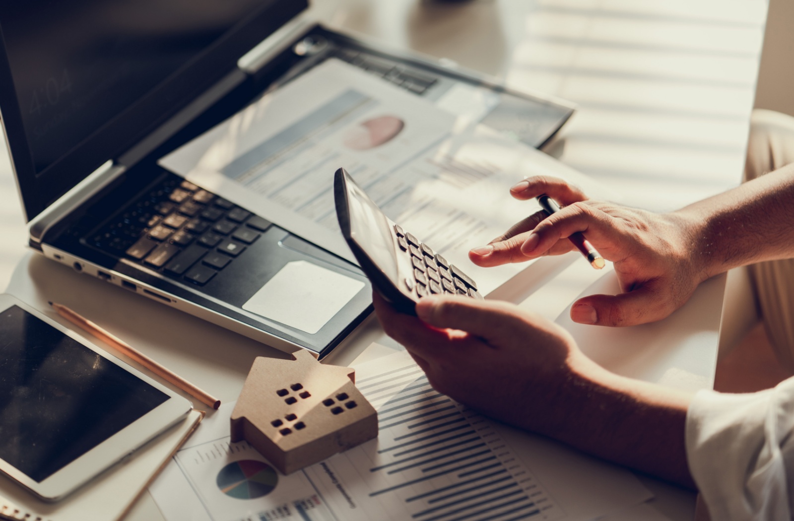 A close-up of a hand calculating a down payment amount on a crowded desk.