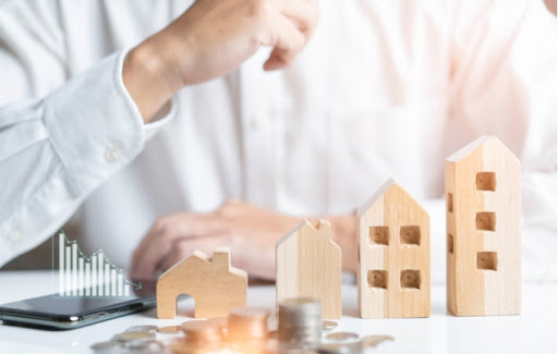 Small model houses and coins laying in front of a person attempting to calculate how much they need for a mortgage down payment