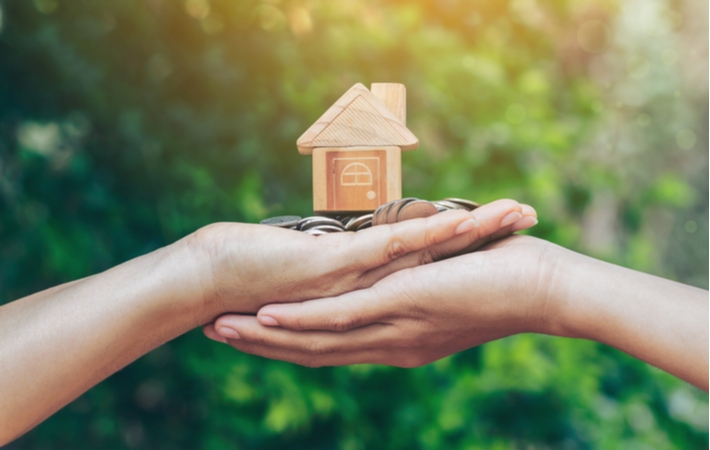 Coins underneath a small wooden, model house symbolizing refinancing a mortgage for home renovations