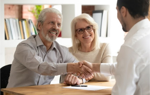 Mature adult couple smiling with the man shaking hands with their male financial advisor after signing an agreement.