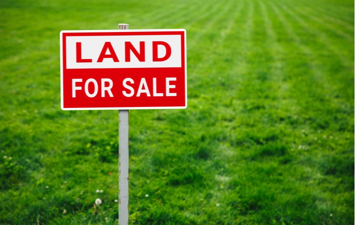 A red and white sign that reads "land for sale" with green grass in the background