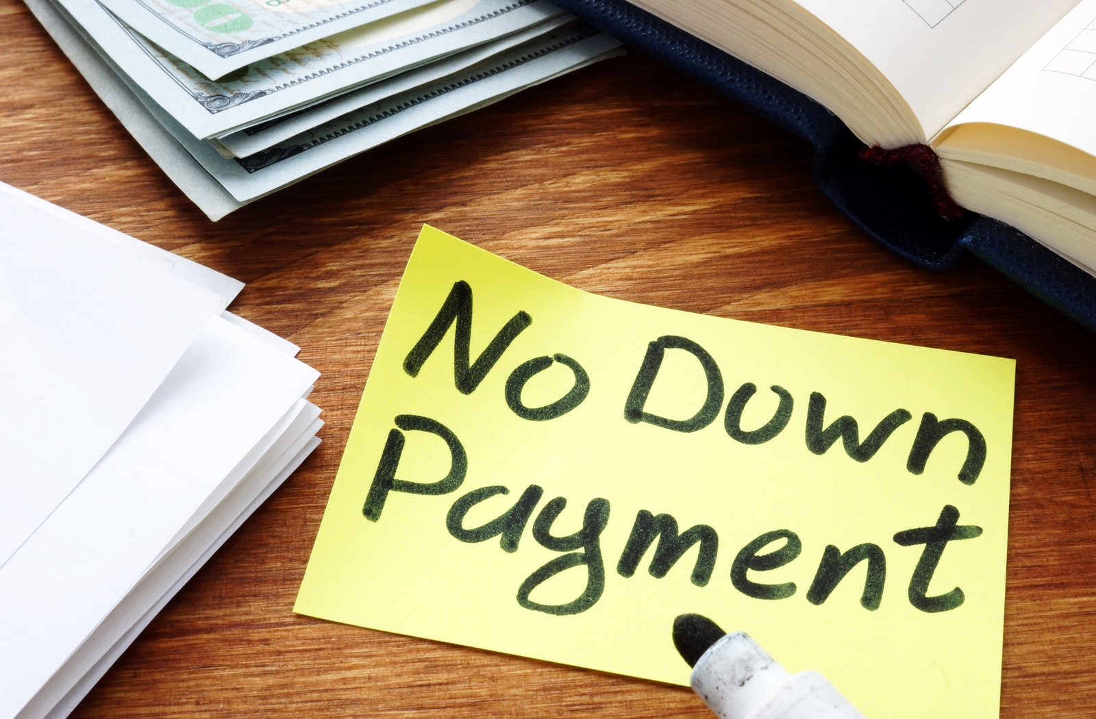 A note laying on a desk with a sharpie that has written "no down payment" on it, surrounded by different pieces of paper and an open book
