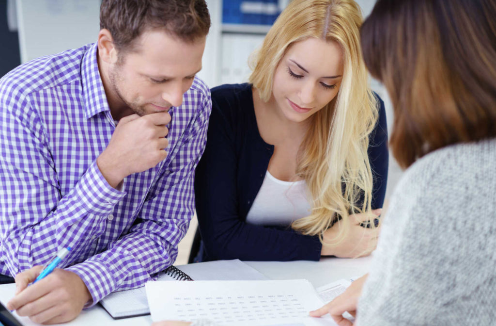 A couple sits across from a mortgage broker while they all look at a form discussing multiple mortgages.