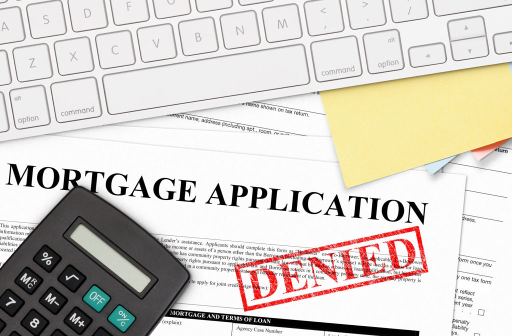 A red denied stamp on a mortgage application on a table with a calculator and a computer keyboard.