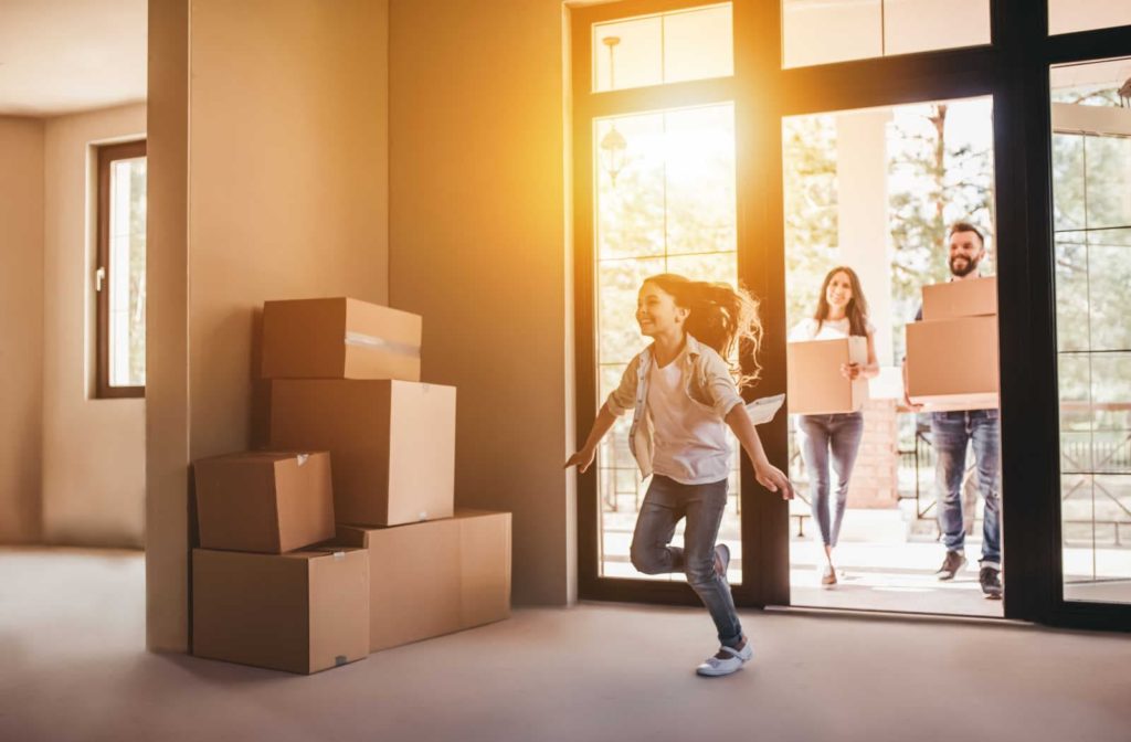 A young girl running into a new home with her parents carrying moving boxes in behind her after getting a mortgage as a non-resident in Canada