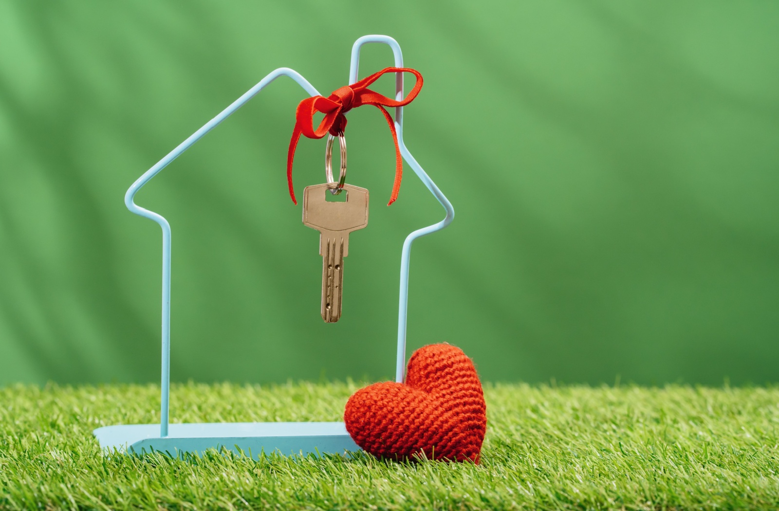 A wire-frame house model with a key tied to it sits on grass.