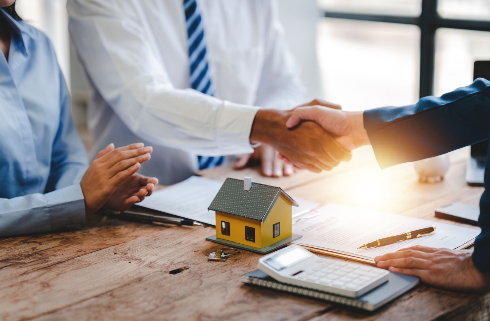 A real estate broker shakes hands with their client over a model of a house.