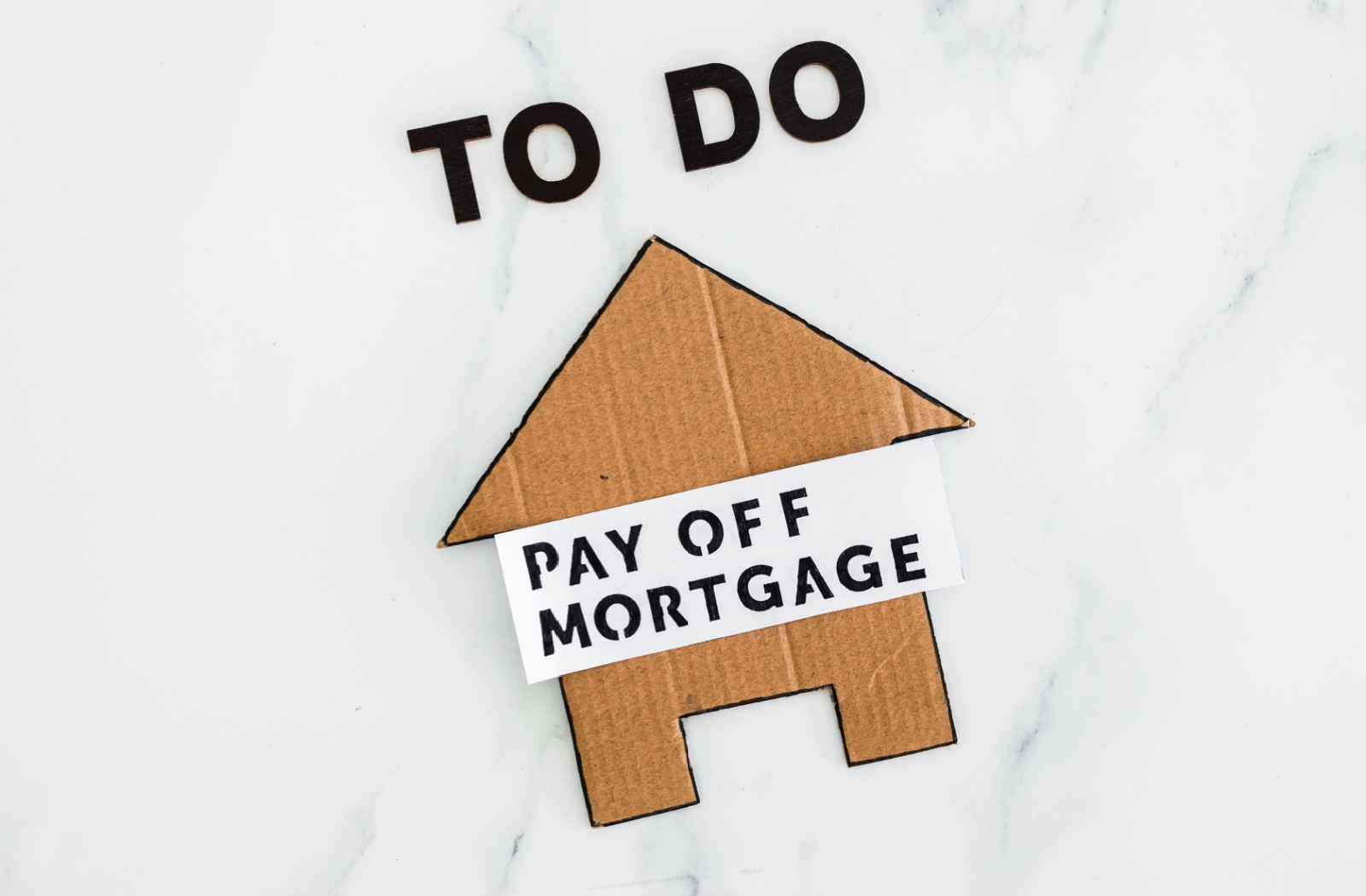 A cardboard house with a note saying "Pay Off Mortgage" sits below a "To Do" reminder.
