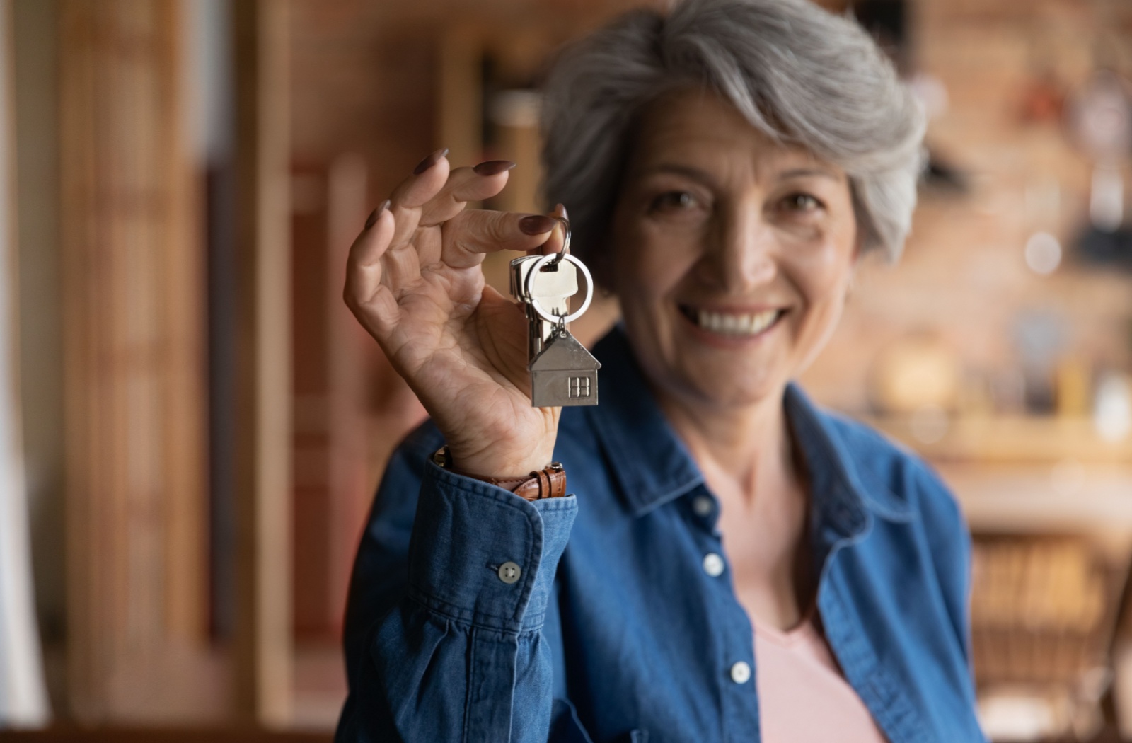 An older adult cheerfully holding the keys to their home.
