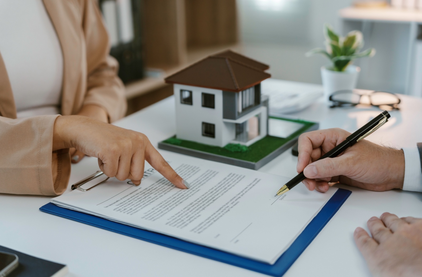 A mortgage broker pointing to mortgage renewal papers on their desk, indicating to the client where to sign.