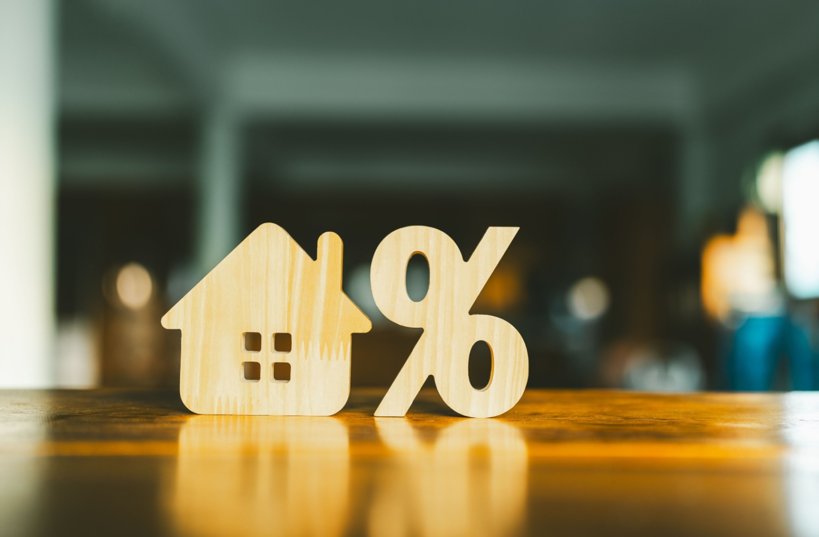 A wood house model sitting on a desk next to a percentage symbol, indicating mortgage interest rate percentages of a open vs. closed mortgage.