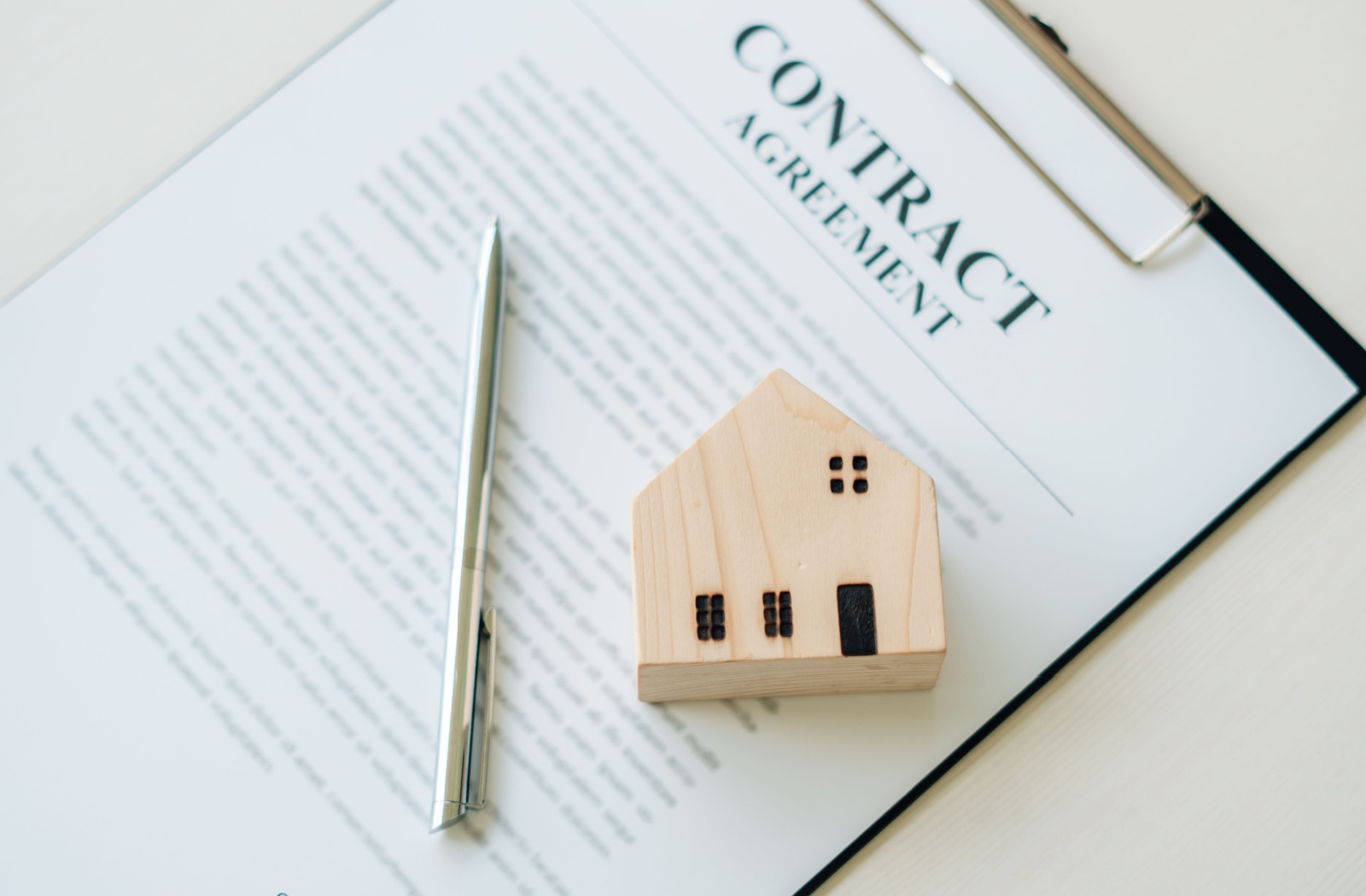 A model house and pen on top of a contract titled "contract agreement" representing that it is a purchase contract.